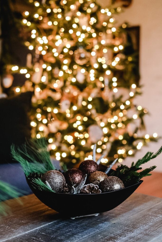 bowl of metallic ornaments on a coffee table with a xmas tree in the background
