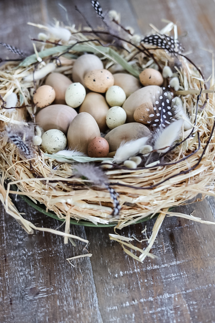 a bird's nest made out of a straw wreath filled with neutral toned eggs