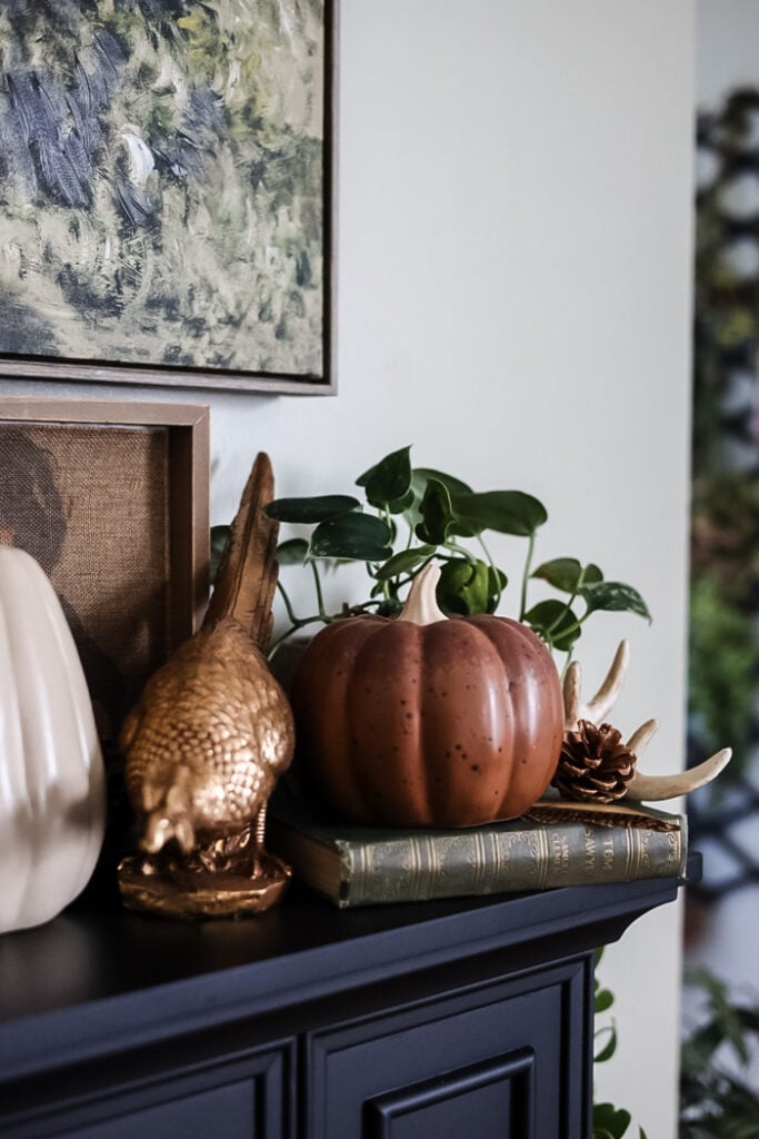 a brown ceramic pumpkin on a mantle with old books, and vintage pheasant statue