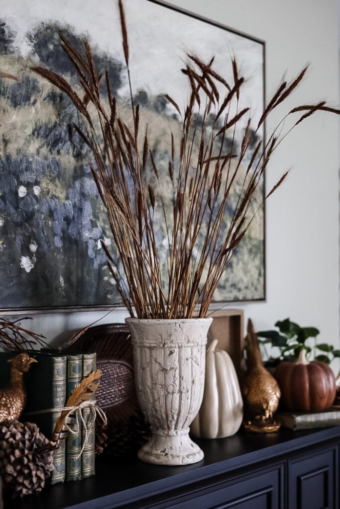 a cream urn vase filled with tall brown ornamental grass styled on a mantle for Fall