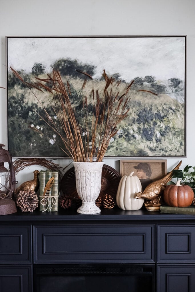 a black fireplace decorated for fall with a variety of vintage and thrifted items, a vase filled with tall ornamental grass.